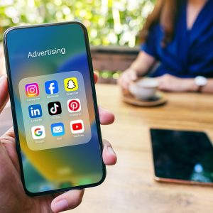 Mockup image of a man holding black mobile phone with blank white screen with woman drinking coffee in cafe